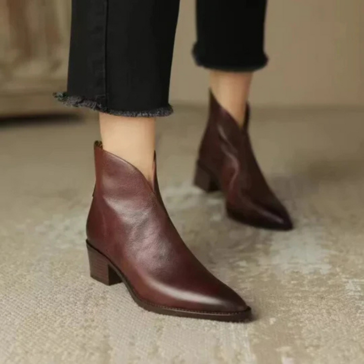 Brown ankle boots with pointed toes, worn with black frayed pants in a neutral indoor setting.