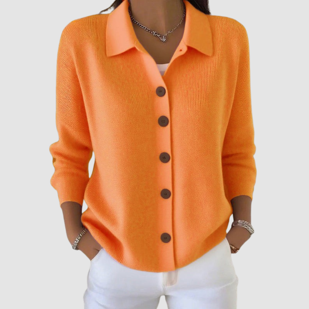 Orange button-up knit cardigan with brown buttons, worn with white pants in a studio setting.