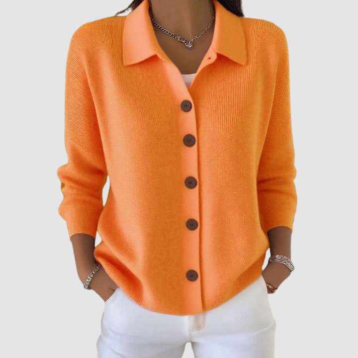 Orange button-up knit cardigan with brown buttons, worn with white pants in a studio setting.