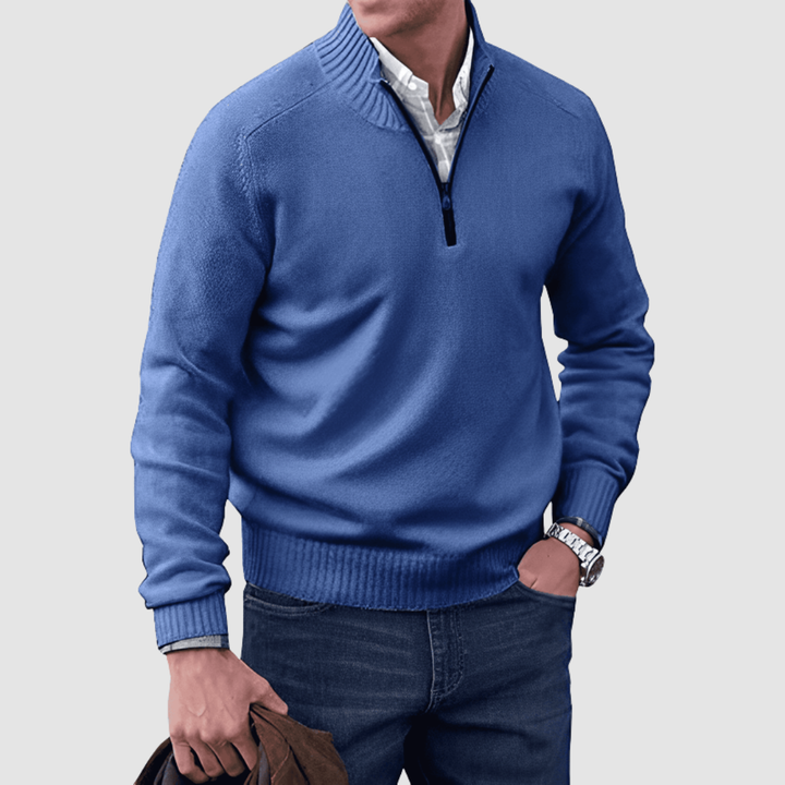 Model in blue zip pullover with ribbed collar and cuffs, holding a jacket. Paired with jeans, set against a plain background.
