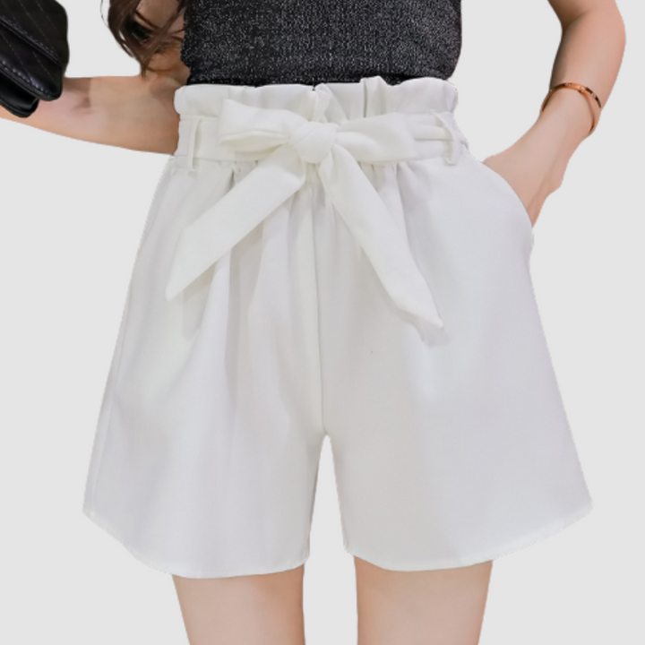 White paperbag waist shorts with a bow, paired with a black glittery top in a studio background.
