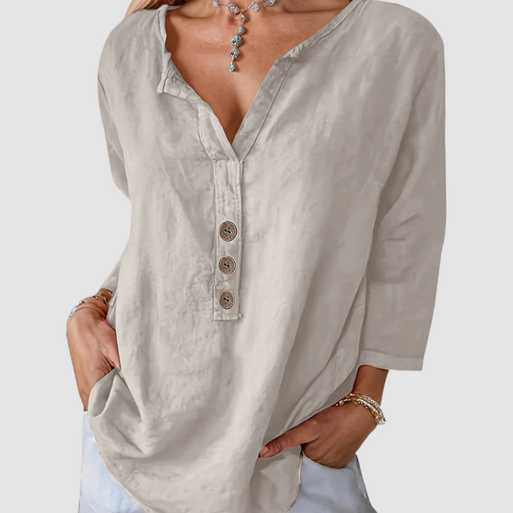 Casual beige blouse with button detail, worn by a model with a necklace, against a plain background.
