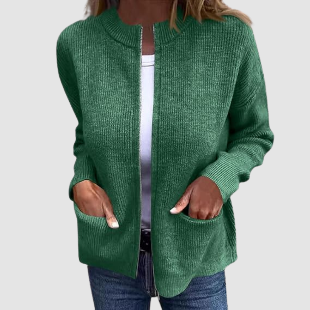 Green cozy cardigan worn over a white t-shirt with hands in pockets. Neutral background.