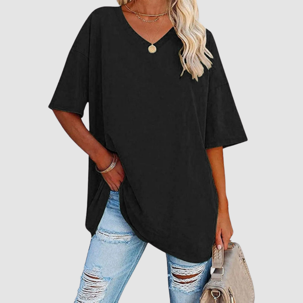 Woman in a black V-neck T-shirt with distressed jeans, holding a beige bag, studio background.
