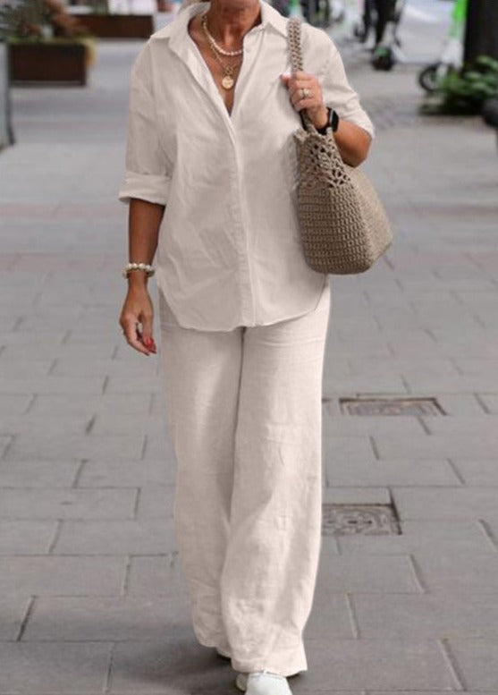 Woman in a light cream two-piece set with rolled cuffs, holding a beige woven bag on a city street.