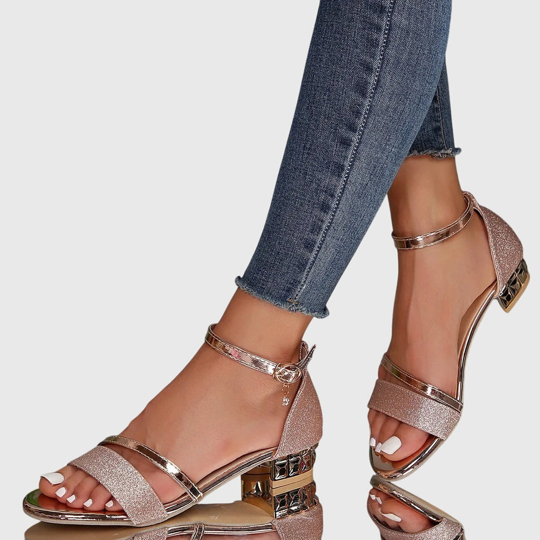 Pink orthopedic heeled sandals featuring glitter and gold accents, styled with frayed hem jeans, on a reflective surface.