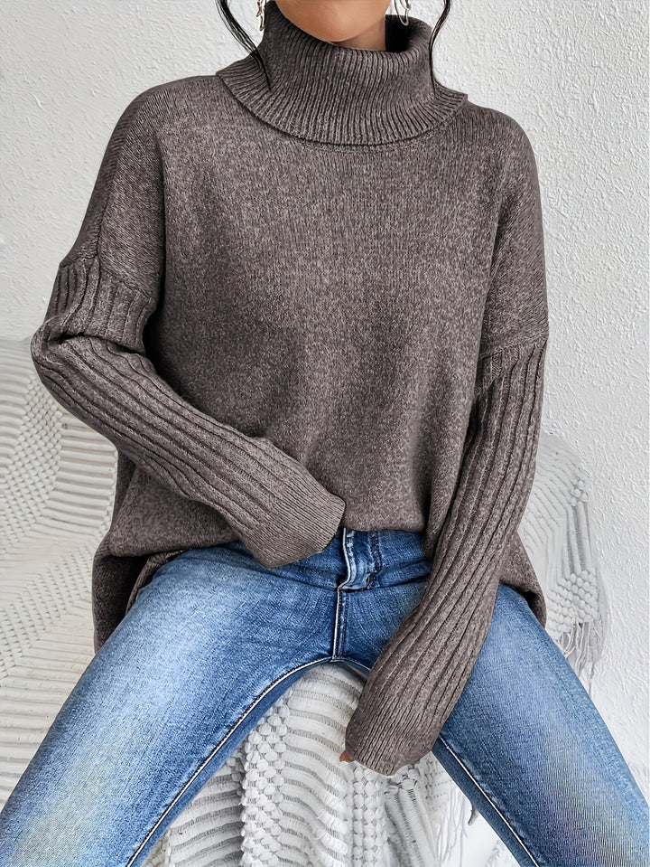 Brown turtleneck sweater with ribbed sleeves, worn with jeans, seated casually on a textured chair indoors.