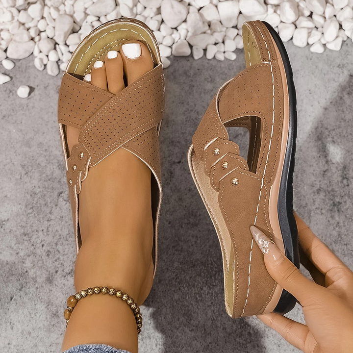 Brown orthopedic wedge sandals viewed from above, placed on a textured surface with white stones.