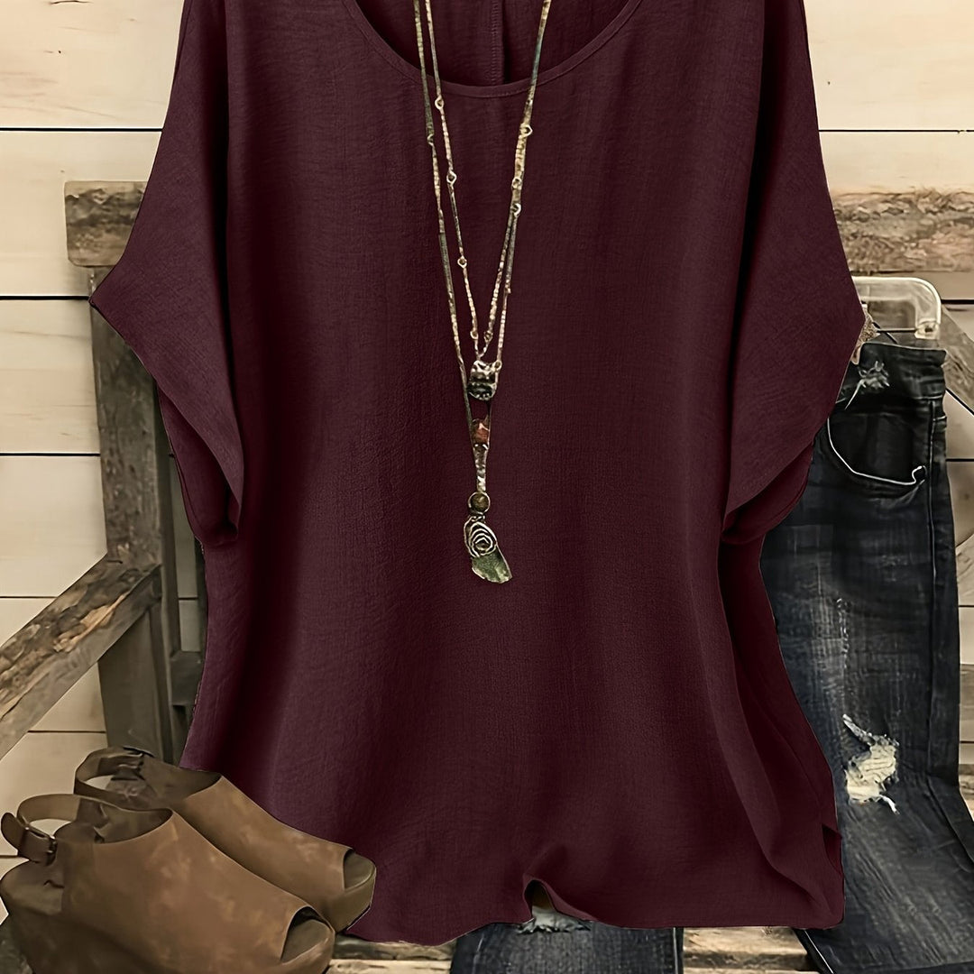 Dark red loose summer top on hanger with necklace, sandals, and jeans on rustic bench.