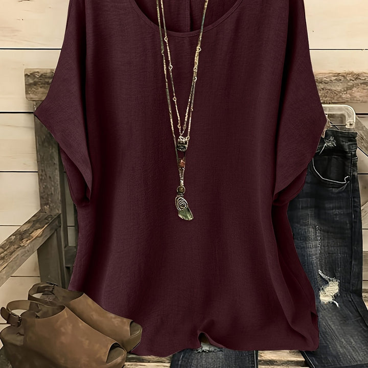 Dark red loose summer top on hanger with necklace, sandals, and jeans on rustic bench.