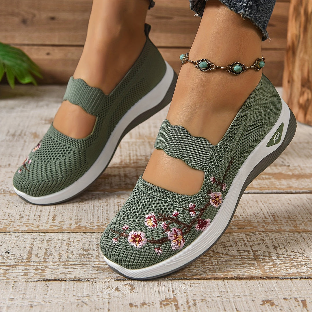 Green orthopedic shoes with floral embroidery, worn with an anklet, on wooden floor background.