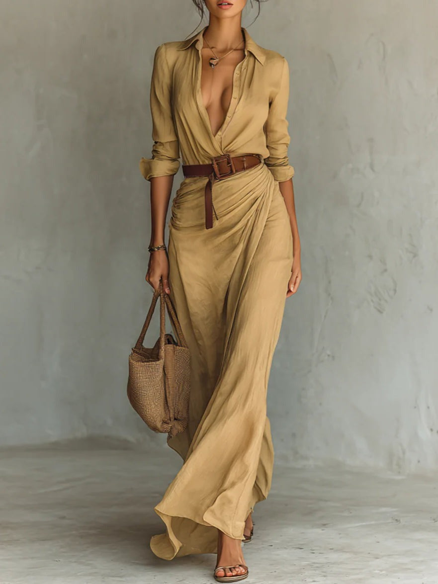 Elegant tan shirt dress with deep neckline, cinched waist with a brown belt. Flowing hem, styled with a woven bag and sandals in a neutral studio setting.