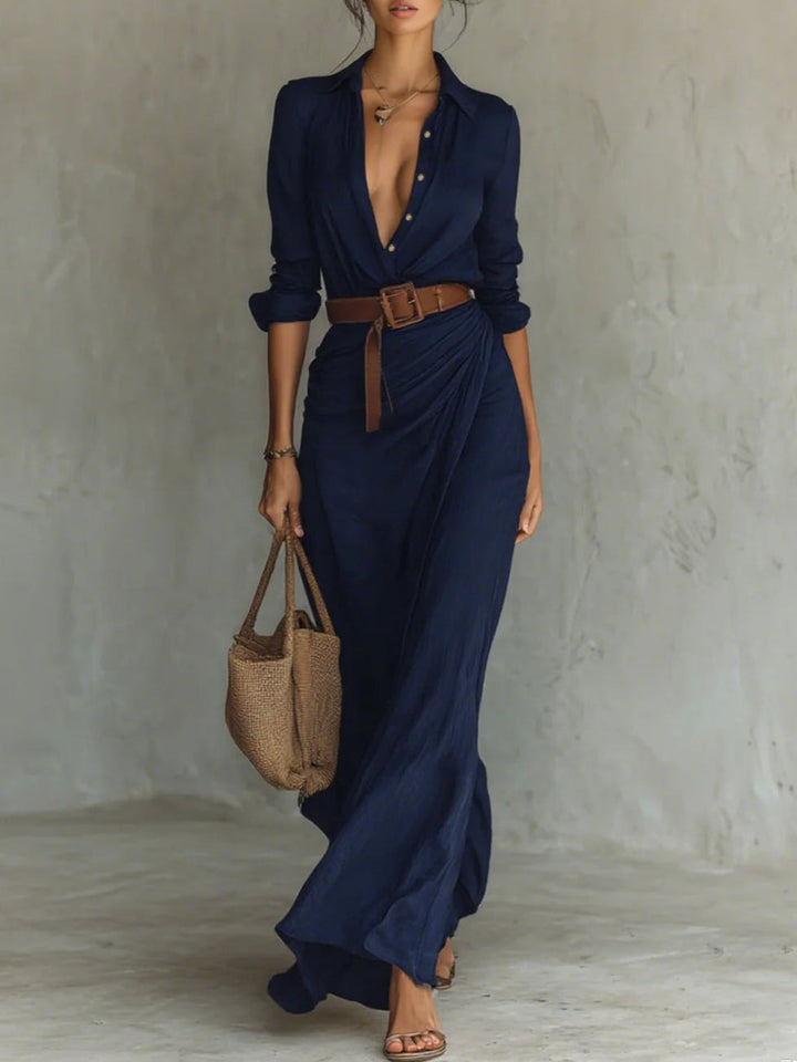 Stylish navy shirt dress with deep neckline and a brown belt at the waist. Flowing hem, accessorized with a woven bag and sandals in a neutral studio setting.