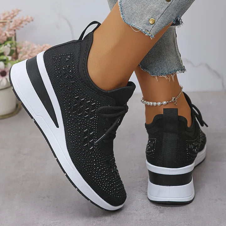Rear view of black orthopedic sneakers with shiny embellishments, worn with jeans in an indoor setting.