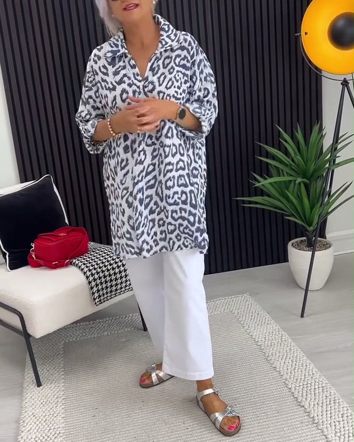 Black leopard print blouse with collar detail, styled with white pants, in a stylish indoor space with decorative accents.