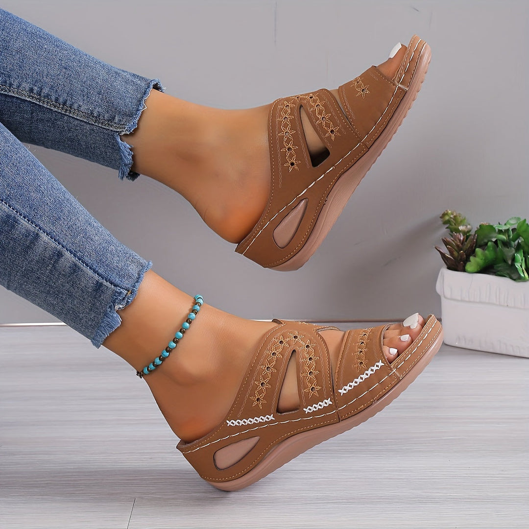 Brown orthopedic sandals with cutout design worn by person with frayed jeans, on a decorative indoor setting.