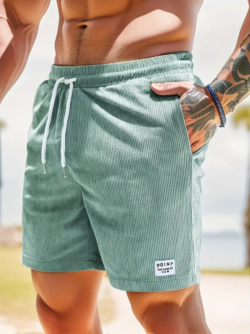 Close-up of green swimming trunks with drawstring, worn by model in outdoor setting.