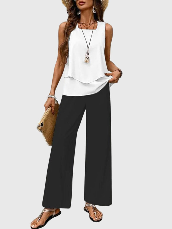 Model in white sleeveless top with layered hem and black wide-leg pants. Neutral backdrop.