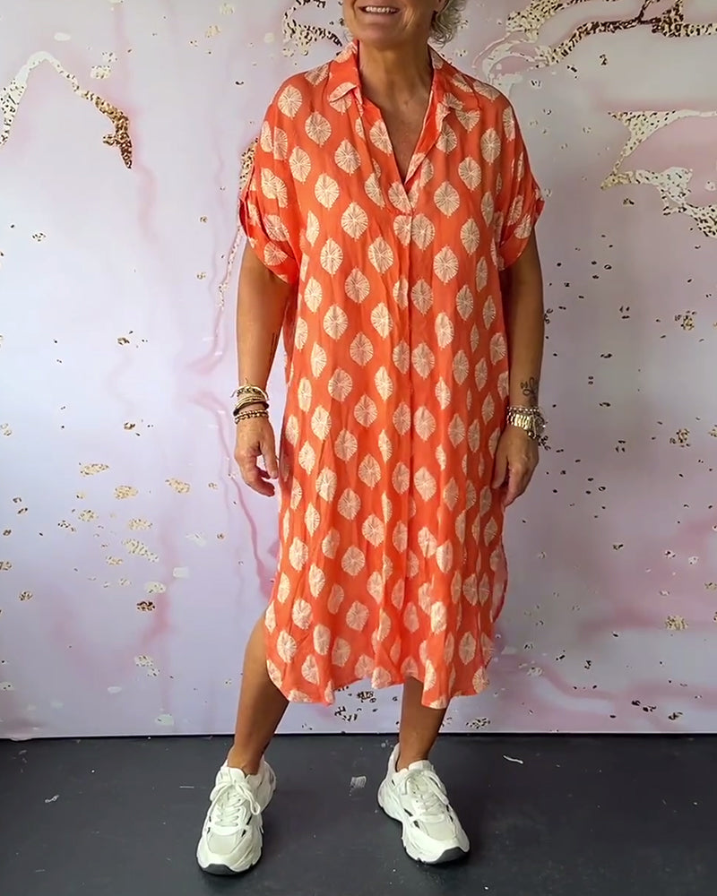Woman in an orange loose lapel collar dress with white leaf patterns, casual sneakers, in studio setting with artistic background.