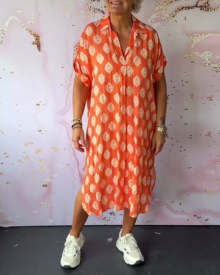 Woman in an orange loose lapel collar dress with white leaf patterns, casual sneakers, in studio setting with artistic background.