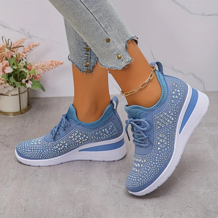 Light blue orthopedic sneakers with intricate design and glitter, worn indoors with jeans and floral decor.