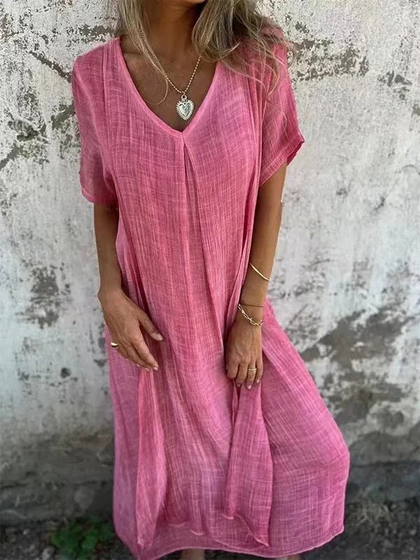 Pink V-neck dress with short sleeves, worn by a person in front of a textured wall.
