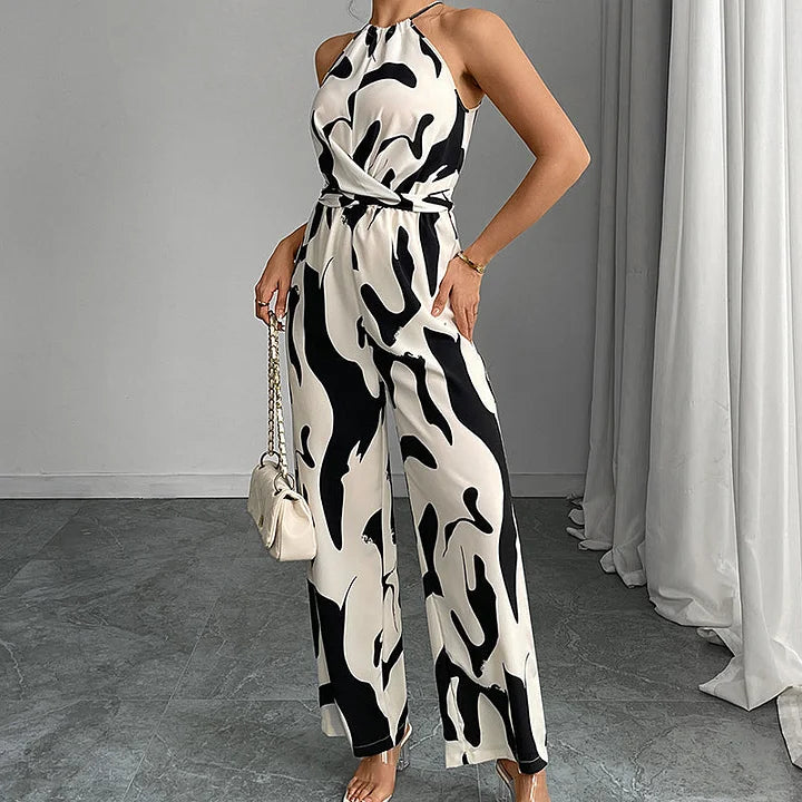 Elegant black and white jumpsuit with abstract patterns, model posing indoors against a soft curtain background.