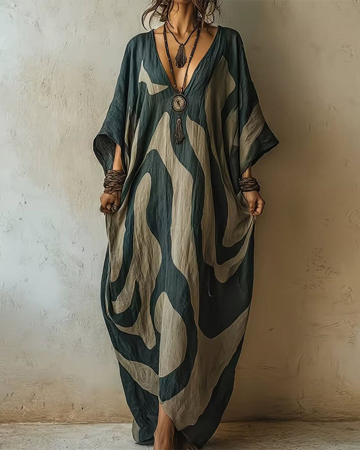 Flowy maxi dress with abstract patterns, deep neckline, rustic jewelry, in a textured indoor setting.
