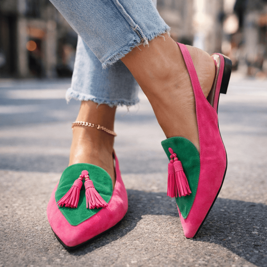 Pink and green sandals with tassels, worn with jeans, urban street background.