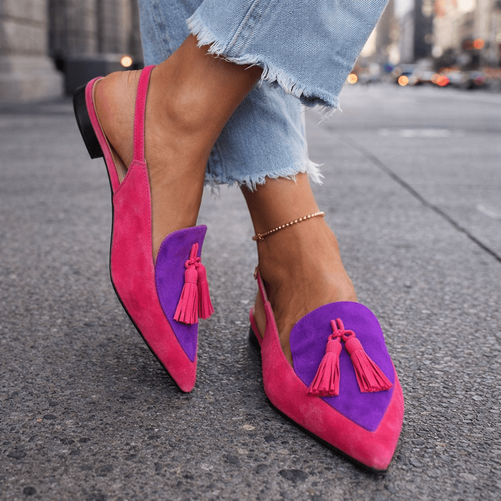 Pink sandals with purple accents and tassels, paired with frayed jeans, city street background.