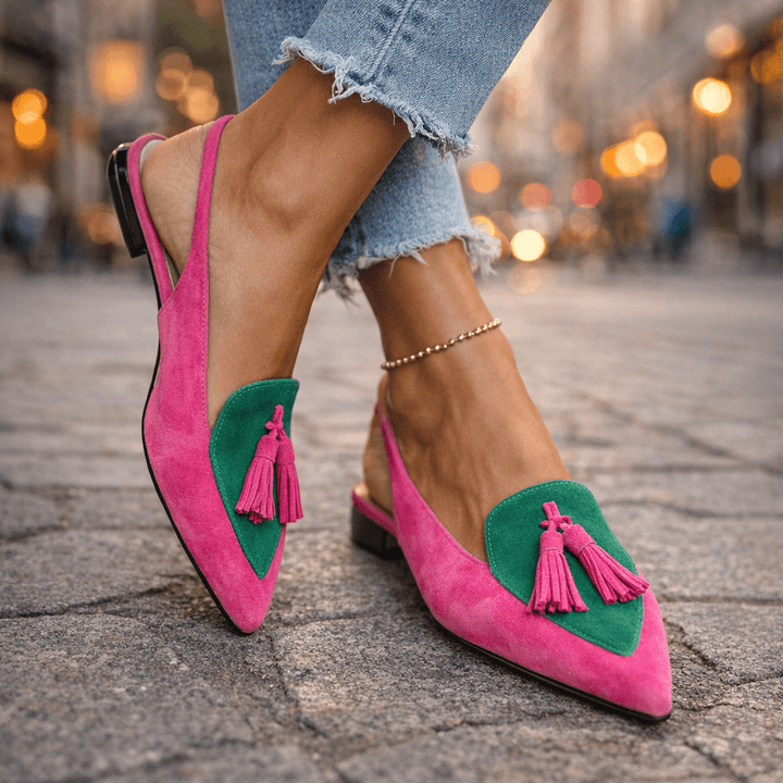 Pink and green sandals with tassels, worn with ripped jeans, on textured pavement.