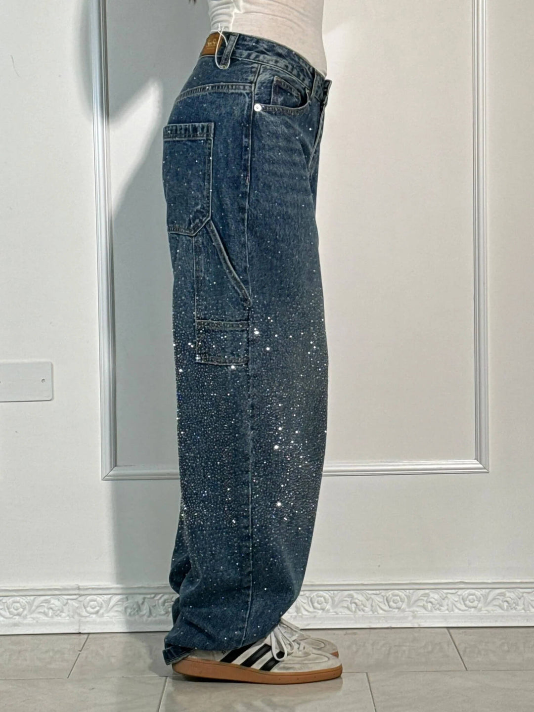 Side view of dark blue glittering trousers with large pocket and striped sneakers in a light studio setting.