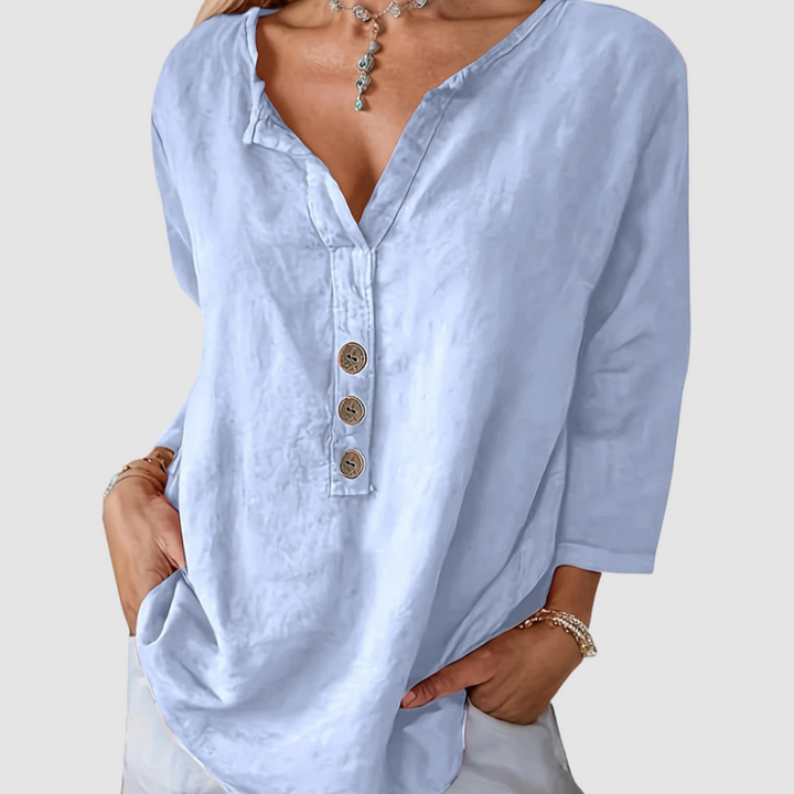 Casual light blue blouse with button detail, worn by a model with a necklace, against a plain background.