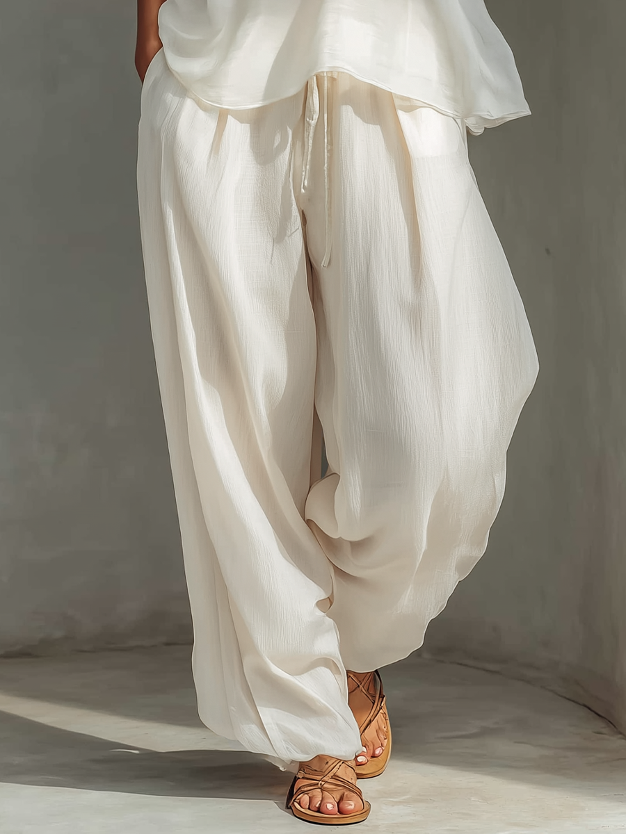 Detail shot of wide-legged white pants and tan sandals on textured gray floor.