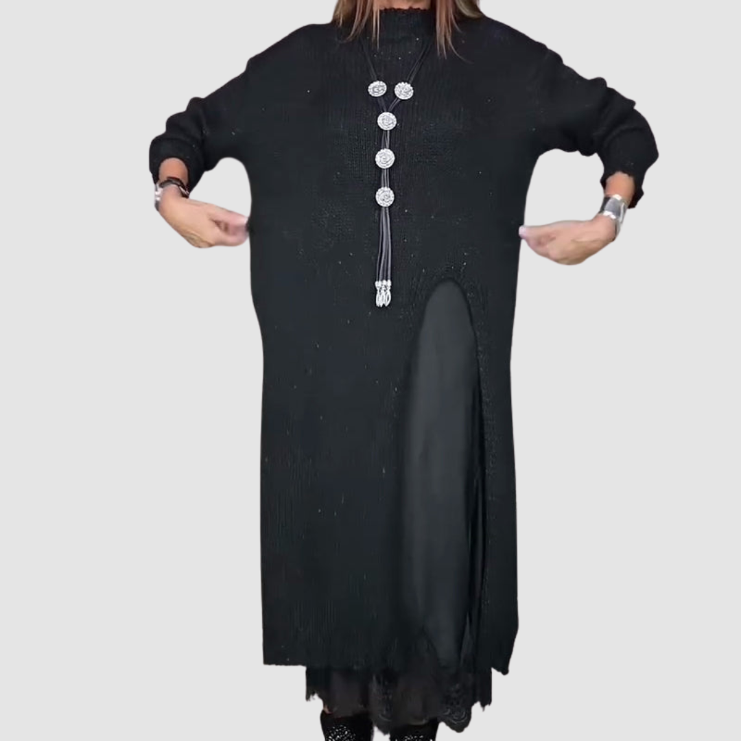Woman stretching sides of a black dress, showing layered design and necklace, against a plain gray backdrop.