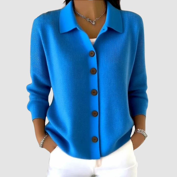 Blue button-up knit cardigan with brown buttons, worn with white pants in a studio setting.