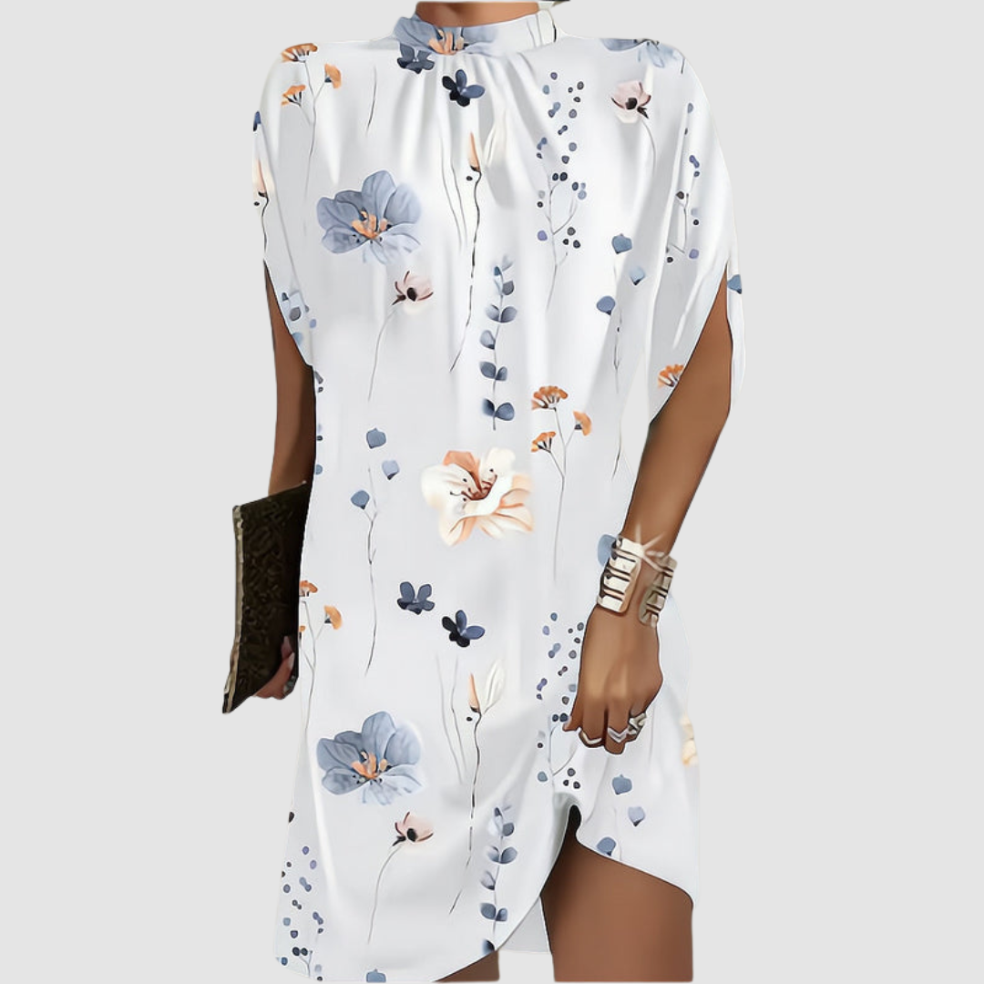 White knee-length dress with floral pattern, loose fit, high neckline, accessorized with gold bangles and clutch on gray background.
