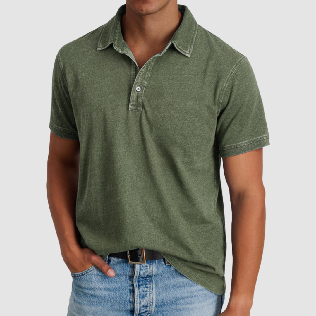 Man in an olive green classic collared polo with short sleeves, button placket, paired with light jeans, studio background.