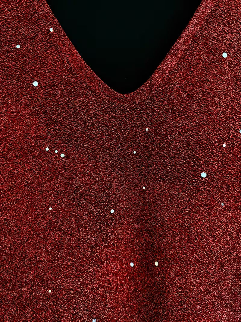 Close-up of a red dress fabric with shimmering detail and V-neckline, highlighting texture and sparkle.