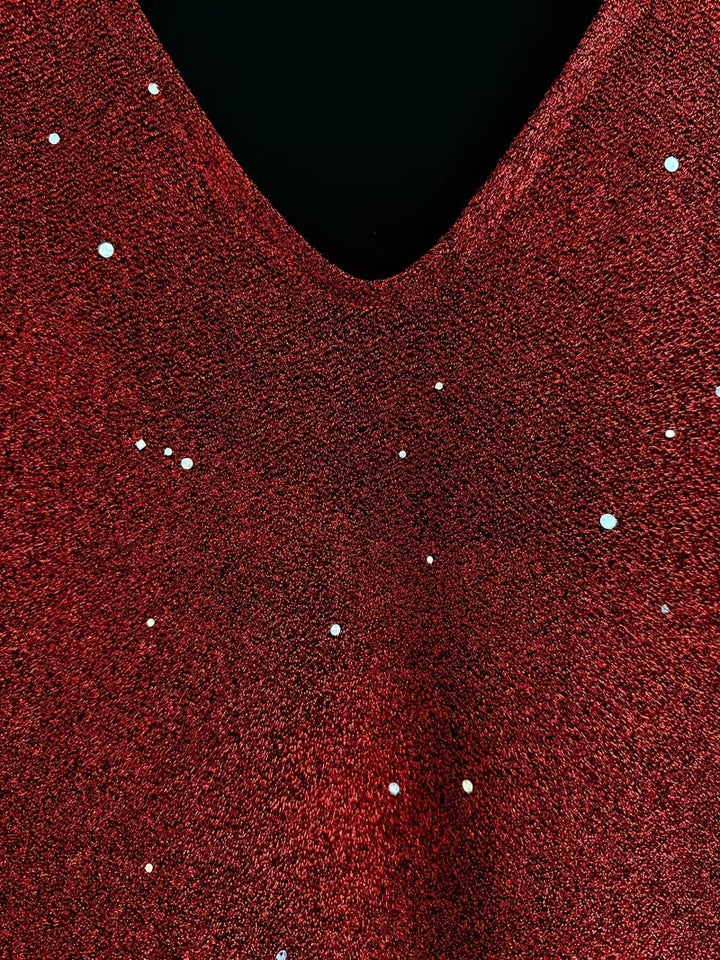 Close-up of a red dress fabric with shimmering detail and V-neckline, highlighting texture and sparkle.