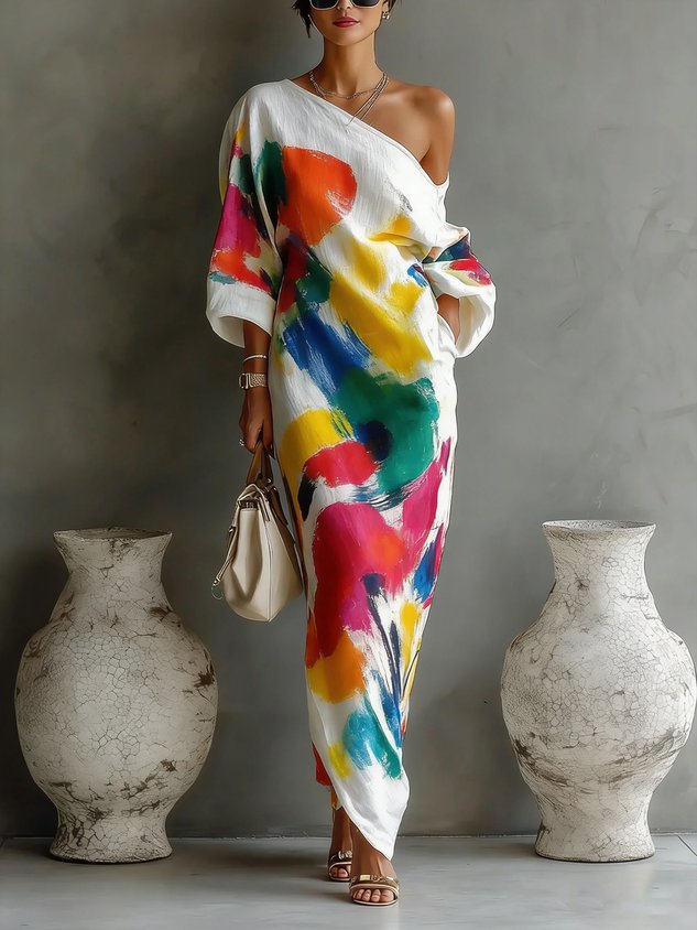 Colorful off-shoulder maxi dress with abstract design and vibrant splashes, styled with a handbag in a minimalistic indoor setting.
