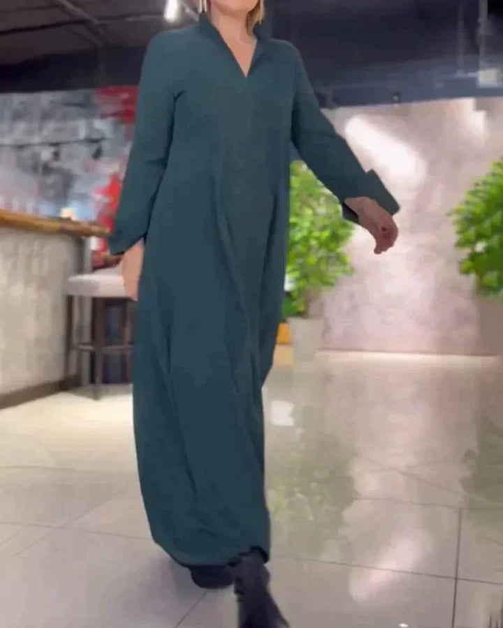 Elegant long dark green dress worn by a person walking indoors with stylish decor and plants.