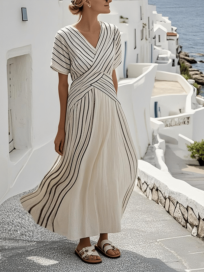 Elegant loose striped maxi dress in white with black stripes, worn outdoors in a coastal, white building-lined street.