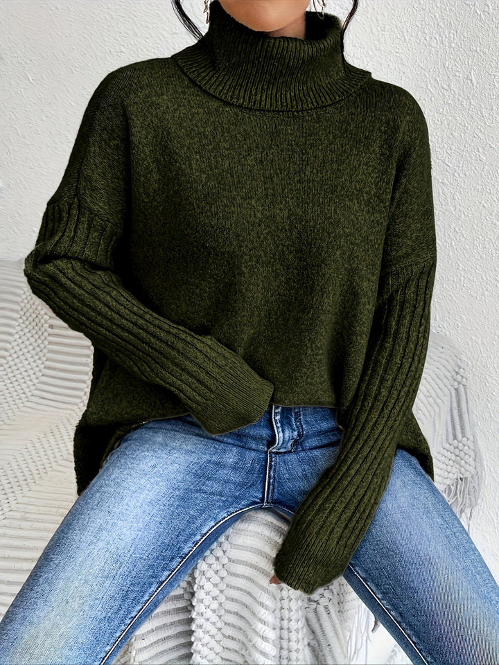 Green turtleneck sweater with long ribbed sleeves, worn with jeans, seated on a textured chair indoors.
