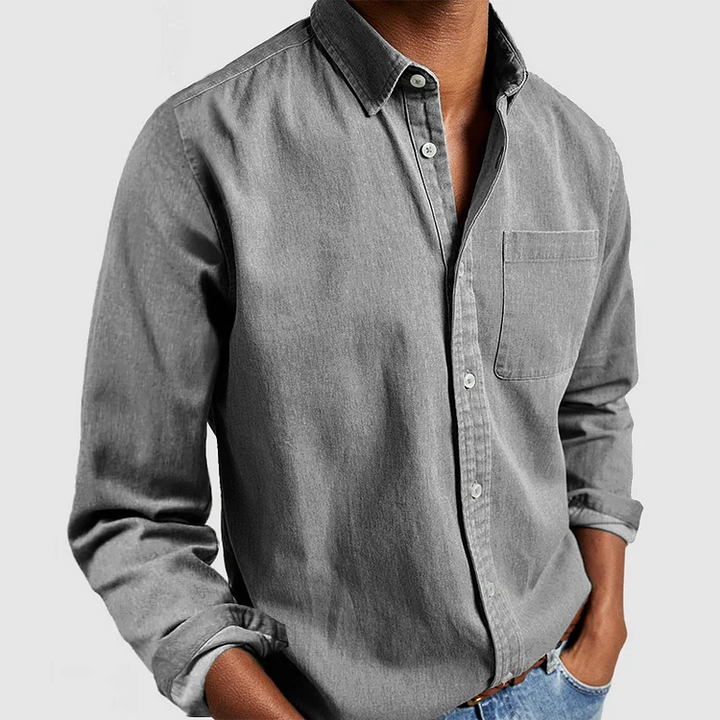 Gray button-up shirt with front pocket and rolled sleeves, styled with hands in pockets; gray background.