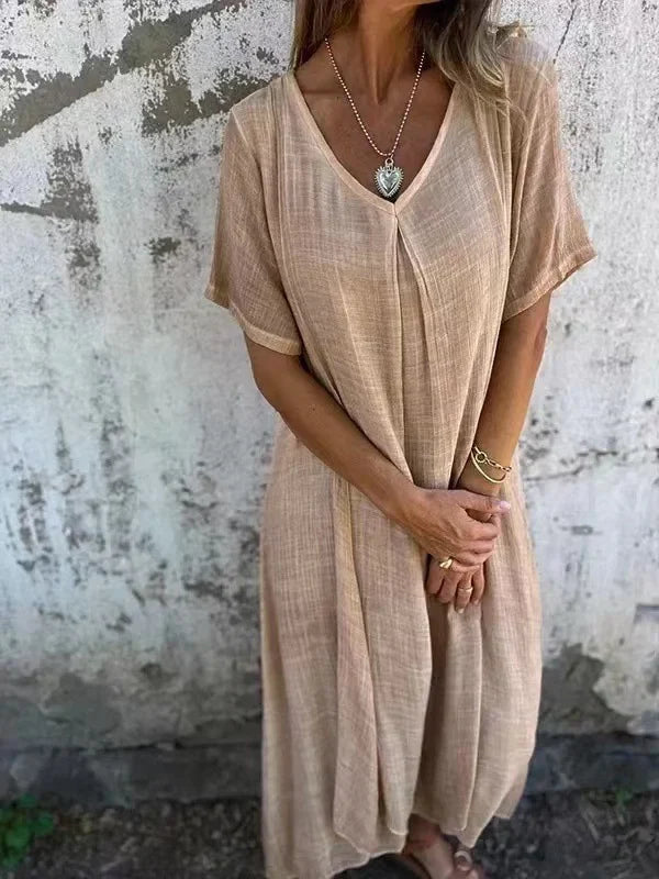 Beige V-neck dress with short sleeves, worn by a person in front of a textured wall.