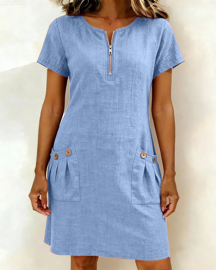 Blue short-sleeve dress with zipper front and buttoned pockets, worn in a studio setting.