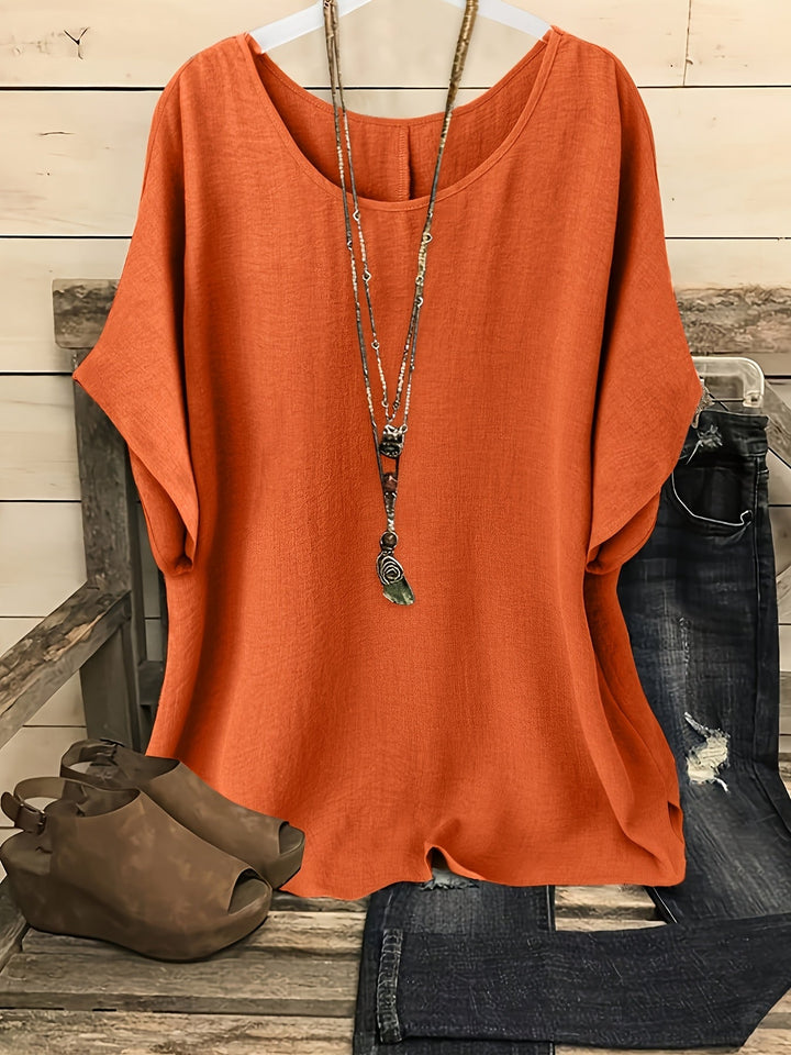 Orange loose summer top on hanger with necklace, sandals, and jeans on rustic bench.