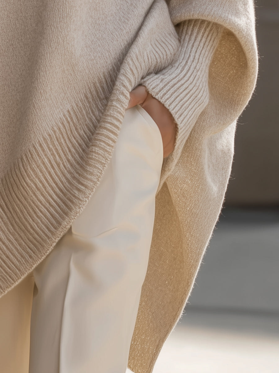 Close-up of a beige sweater sleeve with ribbed detail and a hand in a pocket, in an urban setting.