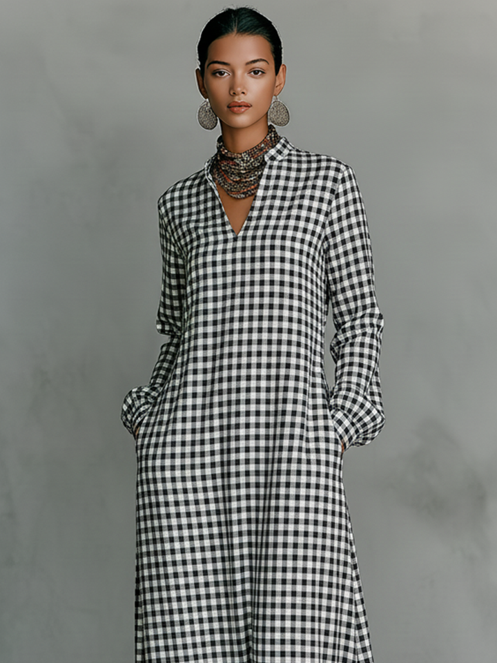 Model wearing black and white plaid V-neck maxi dress with long sleeves, accessorized with earrings and a necklace, in a studio setting.